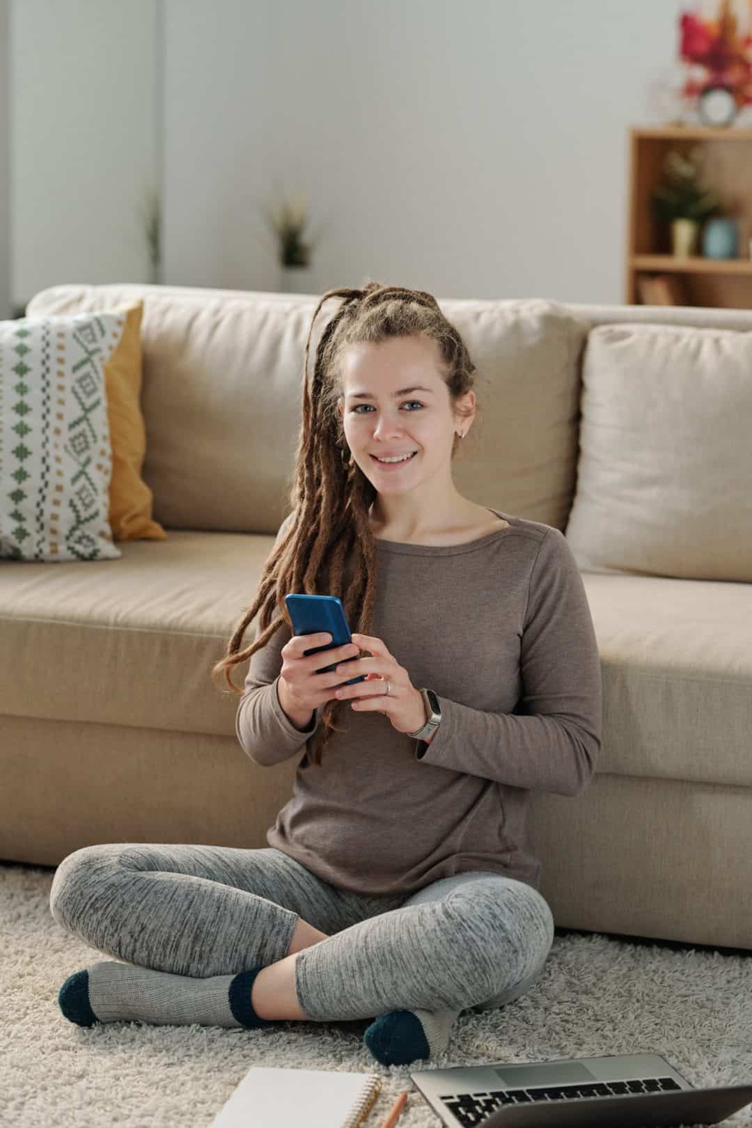 happy-young-woman-with-smartphone-sitting-on-the-floor-by-couch.jpg